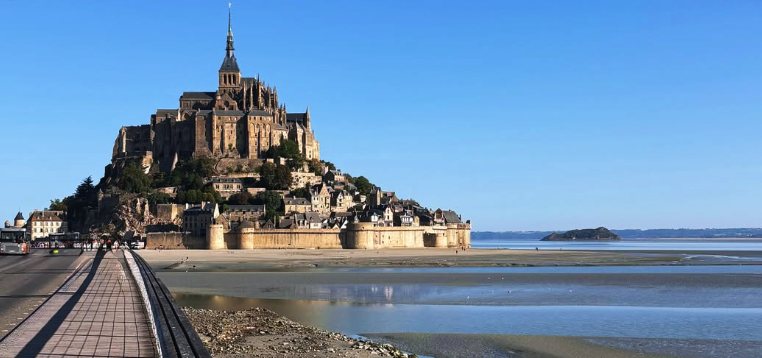 Mont Saint-Michel seen along the causeway at low tide, with the islet of Tombelaine on the horizon