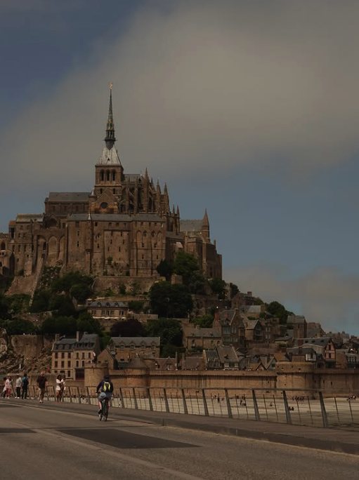 Mont Saint-Michel under evening cloud from the causeway, a cyclist on the road below
